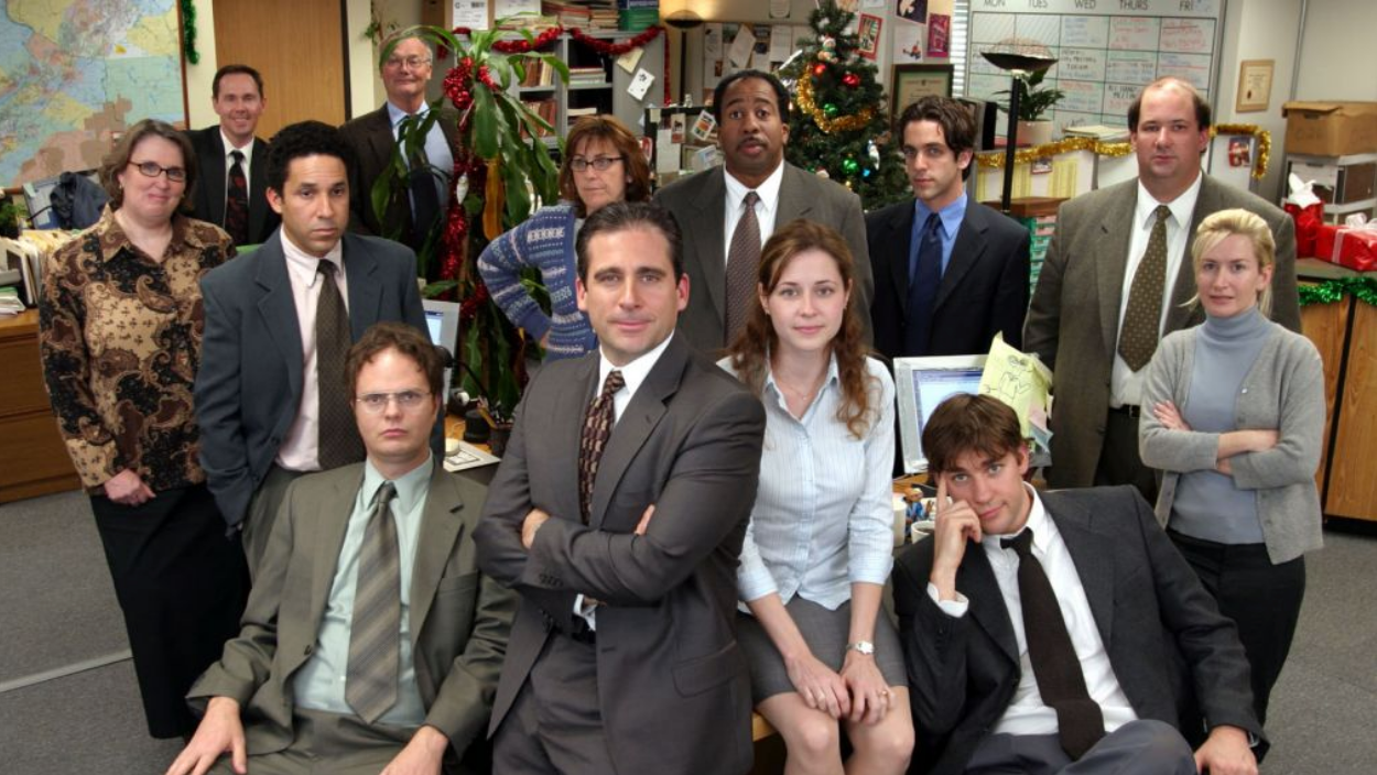 The Office Cast posing in office set with Christmas decorations in the background